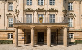 Einladung zur Jahrespressekonferenz des Bundesfinanzhofs am 24. Februar 2026 Sandsteinfarbenes Eingangsportal mit Säulen und Bundesfinanzhof-Wappen