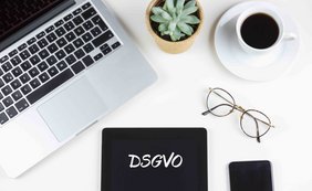 Finanzbehörde muss nicht eidesstattlich versichern Ein Arbeitsplatz mit Laptop, Tasse Kaffee, Pflanze und einem Tablet mit der Aufschrift "DSGVO".