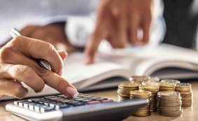 Vollverzinsung nach § 233a der Abgabenordnung (AO) verstößt nicht gegen das Unionsrecht Hände rechnen mit Taschenrechner und Münzen auf Schreibtisch.