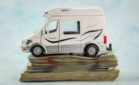 Private Veräußerungsgeschäfte - Auch Wohnmobil im Hochpreissegment kann ein Gegenstand des täglichen Gebrauchs sein Weißes Wohnmobil-Modell, das auf einem hohen Stapel von Geldscheinen steht.